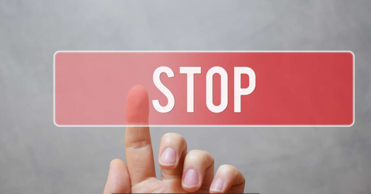 La main d'une personne qui appuie sur un bouton "stop" de couleur rouge avec son index