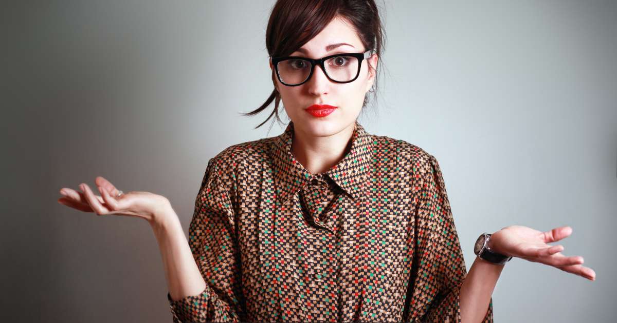 Une femme avec des lunettes et les cheveux attachés mime un "je ne sais pas" avec les coudes levés