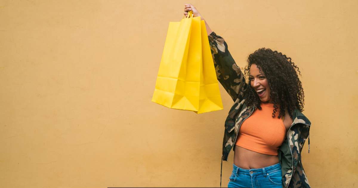 Une femme avec un blouson noir tient un sac de shopping dans sa main droite.